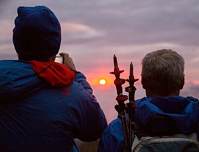 Walkers admire the sunrise from Monte Elmo with the sun rising from the peaks of the Sesto Dolomites