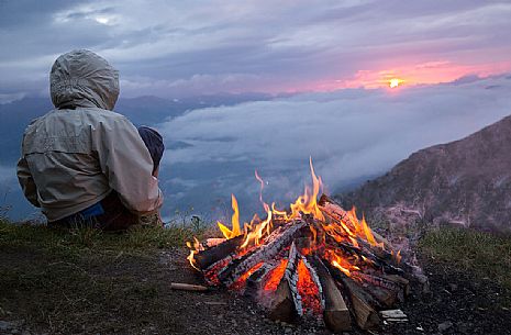 Young trekker can enjoy the sunrise on the Sesto Dolomites from Mount Elmo around a fire