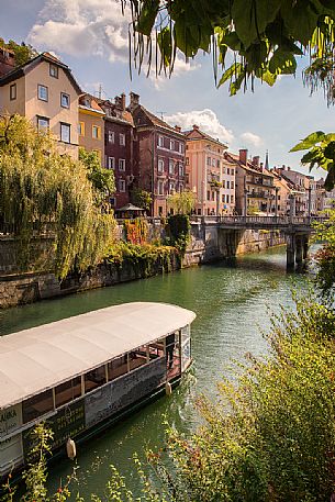 Tourist boat crosses the Ljubljanica river under the gaze of the picturesque houses of Lubiana, Slovenia, Europe