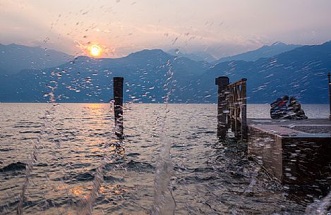 The waves of Lake Garda crash on the shore during a romantic sunset at Malcesine, Italy