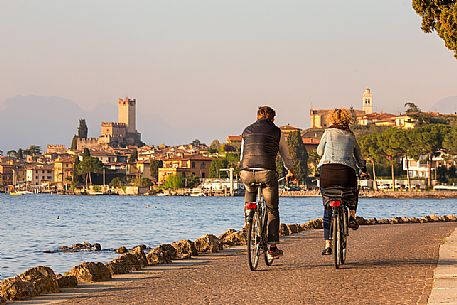 Bicycle couple along Garda lake, in the background the small medieval village of Malcesine, Italy Bicycle couple along Garda lake, in the background the small medieval village of Malcesine, Italy