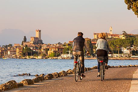 Bicycle couple along Garda lake, in the background the small medieval village of Malcesine, Italy