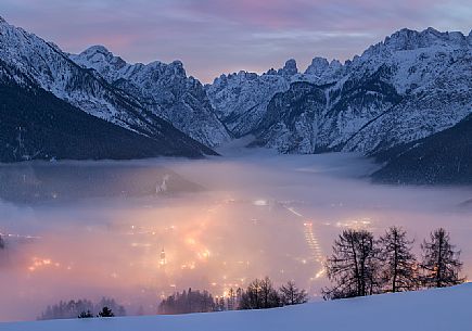 A dense fog dominates the village of Dobbiaco that lights up after sunset, in the background the peaks of Dobbiaco, Piz Popena and Monte Cristallo, Pusteria valley, dolomites, Trentino Alto Adige, Italy, Europe A dense fog dominates the village of Dobbiaco that lights up after sunset, in the background the peaks of Dobbiaco, Piz Popena and Monte Cristallo, Pusteria valley, dolomites, Trentino Alto Adige, Italy, Europe