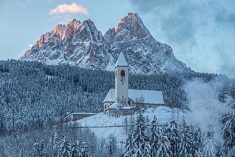 The church of the village of Versciaco after an intense snowfall, in the background the Tre Scarperi peak illuminated at dawn, Innichen, dolomites, Alta Pusteria valley, Trentino Alto Adige, Italy, Europe