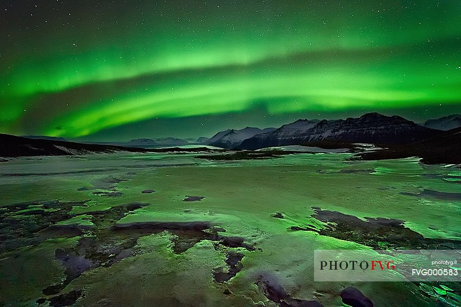 The green shades of the Aurora Borealis reflect on a frozen stream at Jokulsarlon