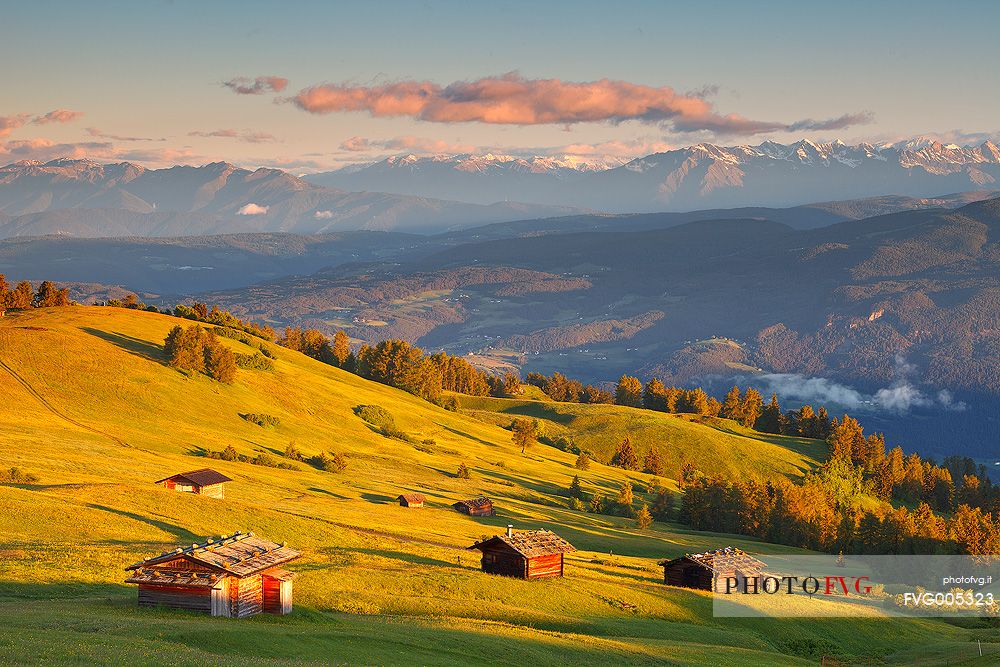 Some little shelters on Alpine meadows of Siusi Alp are illuminated by the warm light of the sunrise