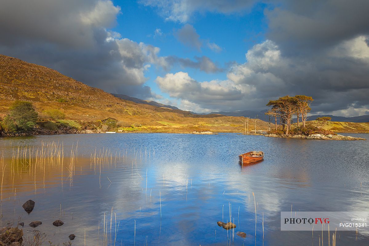 The fishermans boats anchored on the shore of the fascinating Loch Assynt and a beautiful isle of pines on the lake