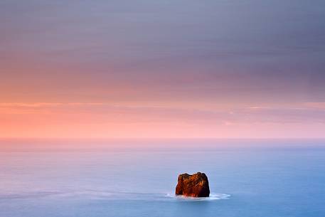 A rock emerges from the waters in the sea and gets inundated by the morning light.