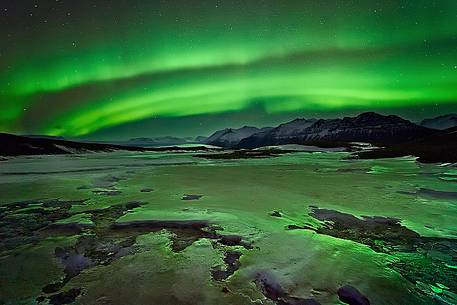 The green shades of the Aurora Borealis reflect on a frozen stream at Jokulsarlon