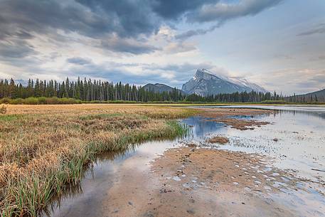 Mount Rundle is reflected into the water of Vermillion Lake during a grey day