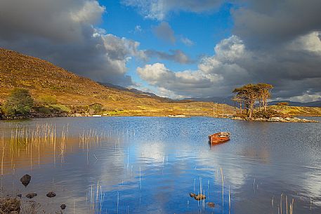 The fishermans boats anchored on the shore of the fascinating Loch Assynt and a beautiful isle of pines on the lake