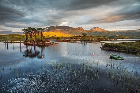 The fishermans boats anchored on the shore of the fascinating Loch Assynt and a beautiful isle of pines on the lake