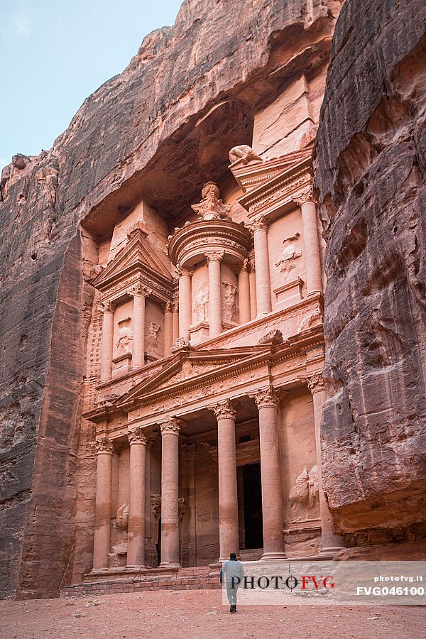 A man walks towards the Treasury or El Khasneh facade in a cloudy day in Petra, Jordan