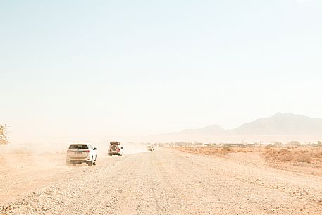 Four 4x4 cars driving in the dust on a gravel road, on the way to Sesriem, Namib Naukluft National Park, Namibia. Africa