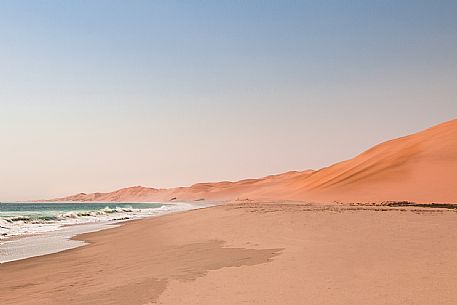 Namib desert orange sand dunes meet the waves of Atlantic ocean on the coast of Namibia at Sandwich Harbour, Walvis Bay, Namibia, Africa