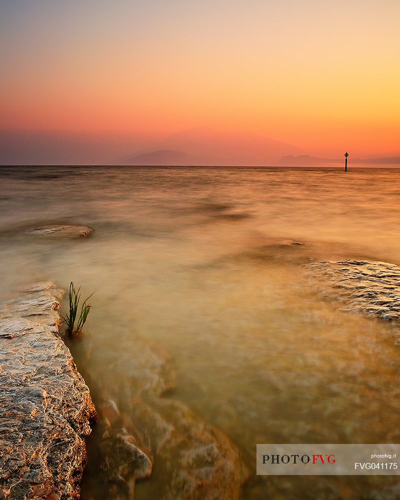 Garda Lake from Sirmione coast at sunrise. At the horizon the shapes of Mount Baldo.