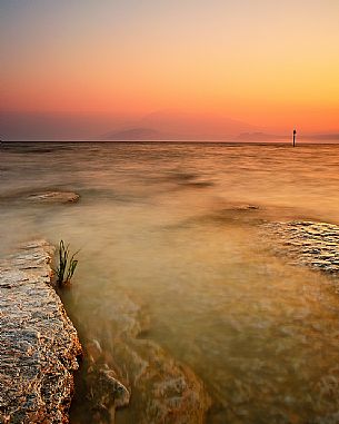 Garda Lake from Sirmione coast at sunrise. At the horizon the shapes of Mount Baldo.