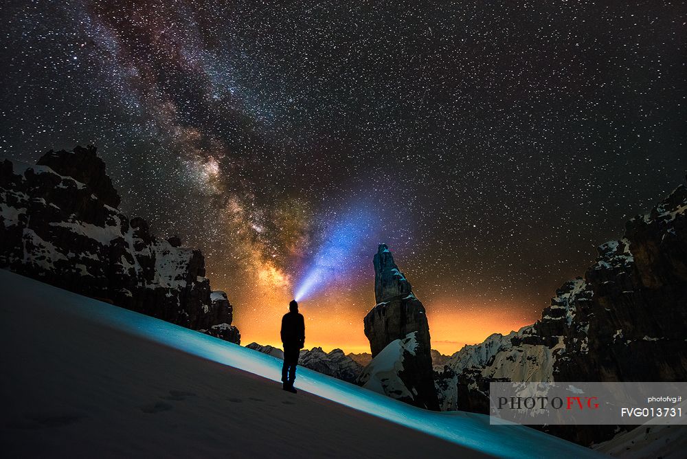 A hiker at night, wearing a head torch with in the background the famous Campanile di Val Montanaia