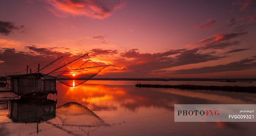 Sunset on salt lake in Ravenna whit pier, boat and fishing huts