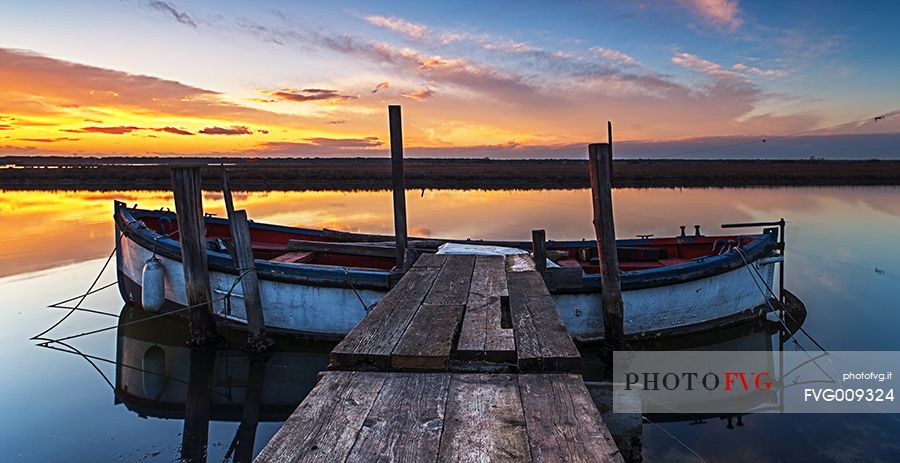 Sunset on salt lake in Ravenna whit pier, boat and fishing huts