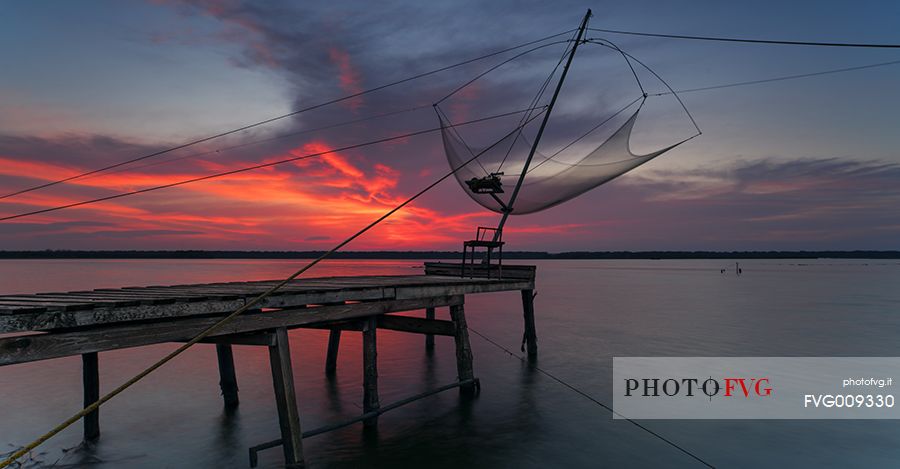 Sunset on salt lake in Ravenna whit pier, boat and fishing huts