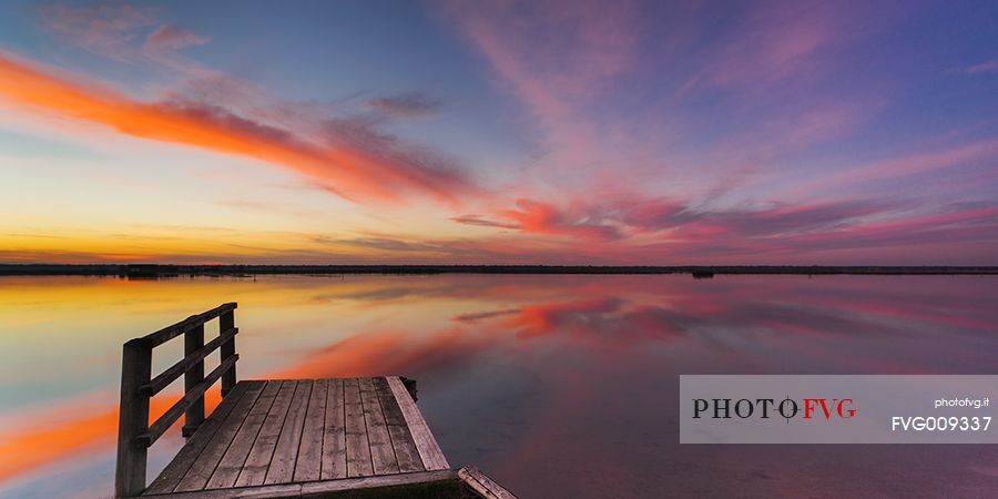 Sunset on salt lake in Ravenna whit pier, boat and fishing huts