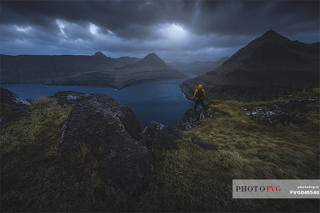 Hiker looking the stormy sunset in the Fjord near Funningur, Eysturoy Island, Faeroe Islands, Denmark 