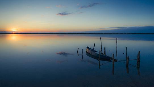 Sunset on salt lake in Ravenna whit pier, boat and fishing huts