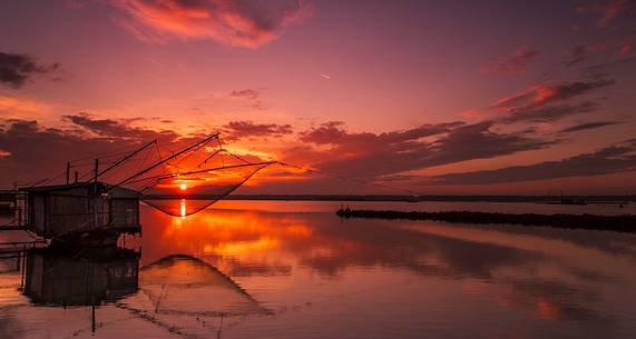 Sunset on salt lake in Ravenna whit pier, boat and fishing huts