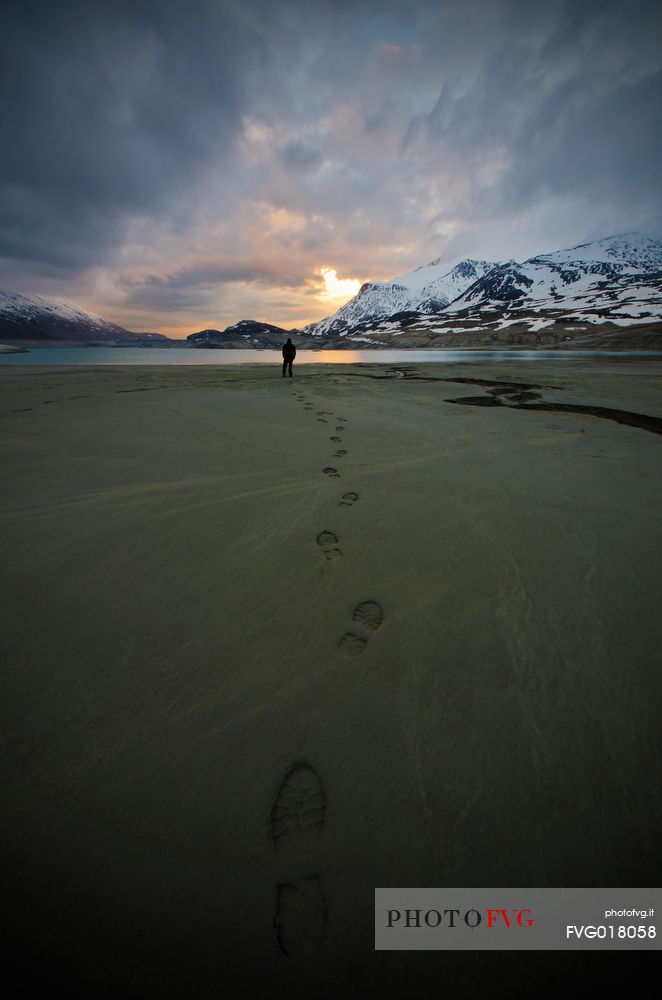 A person in front of the bank of the Mont Cenis lake leaves footprints on his path on the sandy bottom