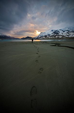 A person in front of the bank of the Mont Cenis lake leaves footprints on his path on the sandy bottom