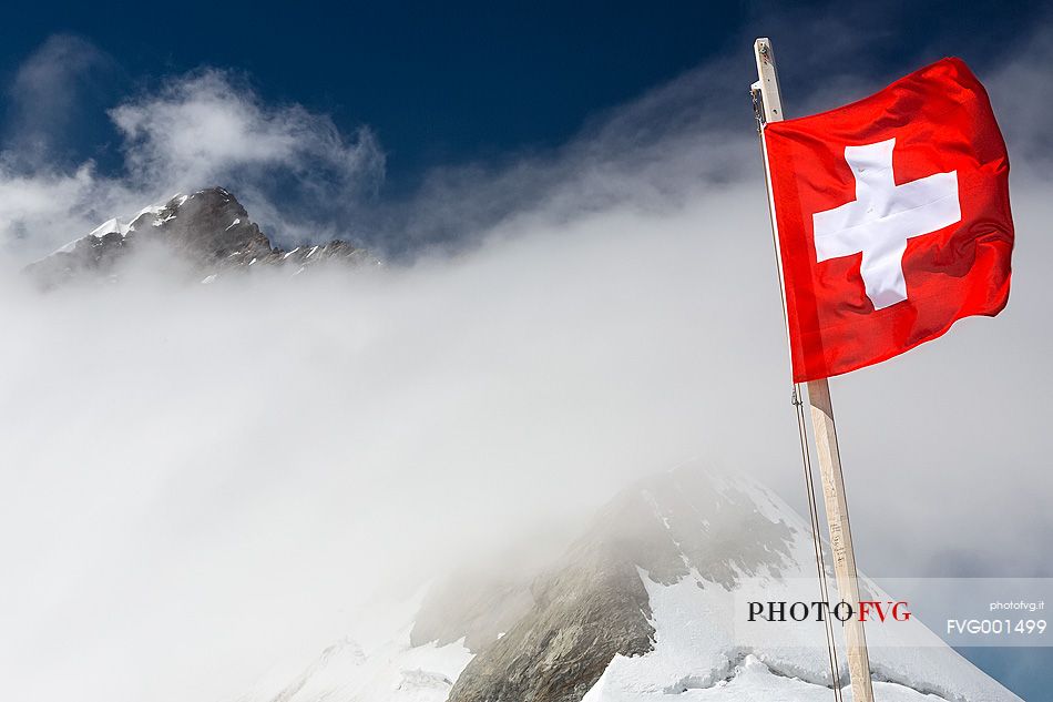 Swiss flag on top of Jungfraujoch , the highest railway station in the Alps, in the background the Jungfrau peak,  Bernese alps, Switzerland, Europe