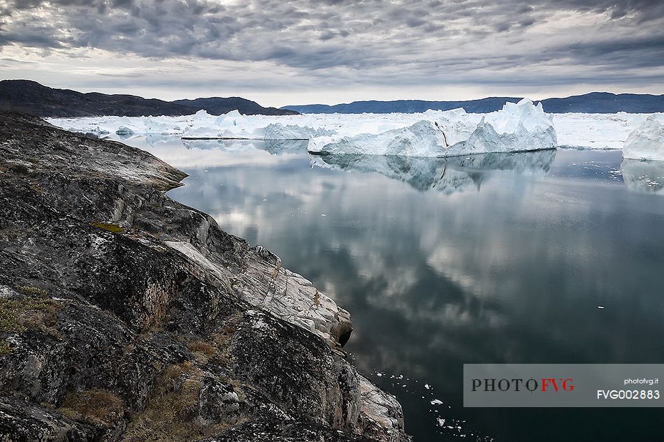 Morning light on icebergs and their reflection on water of Kangerlua Fjord at dawn