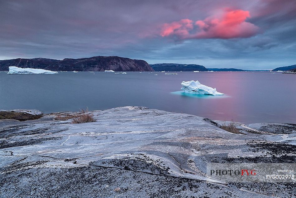 Pink clouds above iceberg in the sea in front  of Ataa a small village of fishermen and seal hunters which was abandoned in the 50s