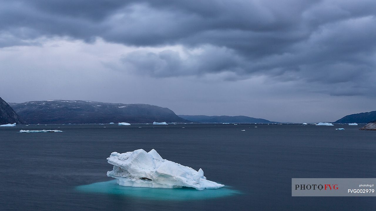 Dark clouds above iceberg in the sea in front  of Ataa a small village of fishermen and seal hunters which was abandoned in the 50s