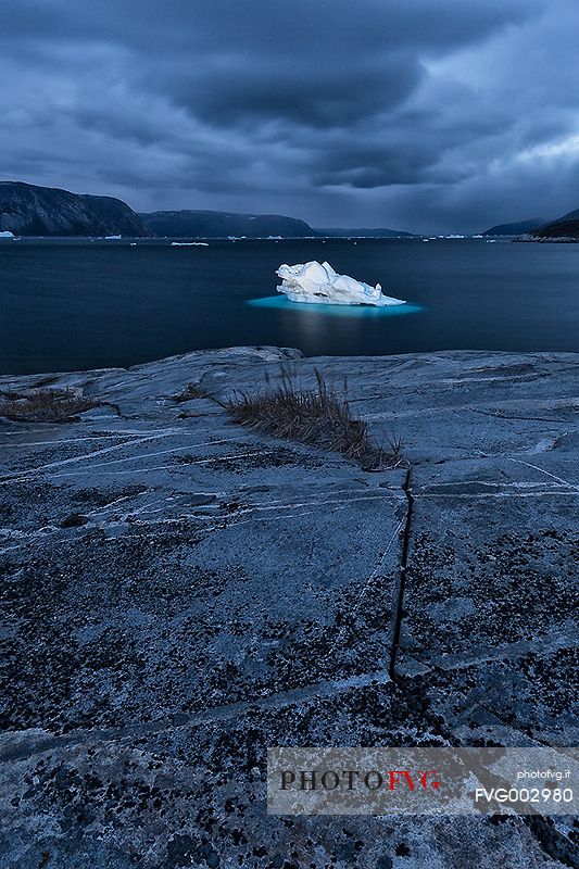 Dark clouds above iceberg in the sea in front  of Ataa a small village of fishermen and seal hunters which was abandoned in the 50s