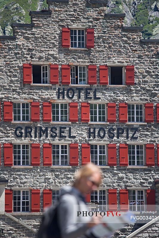 Tourist in front of Grimsel Hospice historic alpine hotel at Grimsel Pass, Bernese alps, Switzerland, Europe