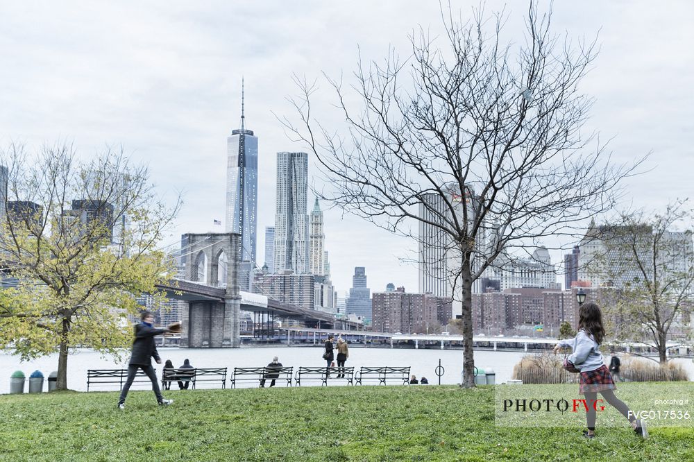 Mother and child relaxing playing baseball; in the background the famous Manhattan skyline with Brooklyn bridge