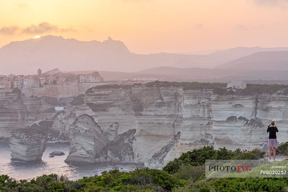 Aa young woman photographs the village of Bonifacio at sunset