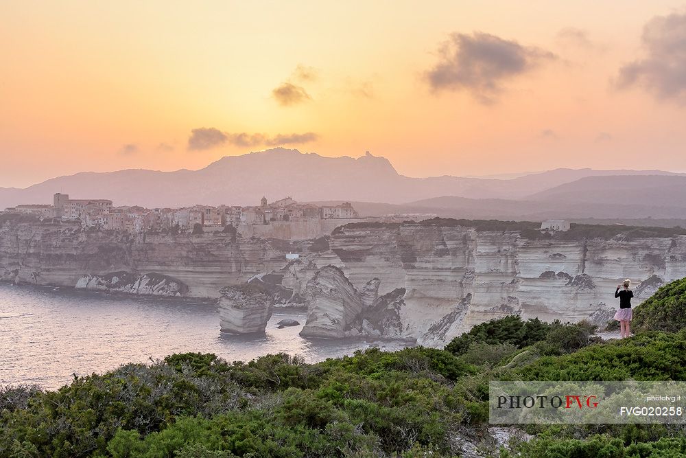 Aa young woman photographs the village of Bonifacio at sunset