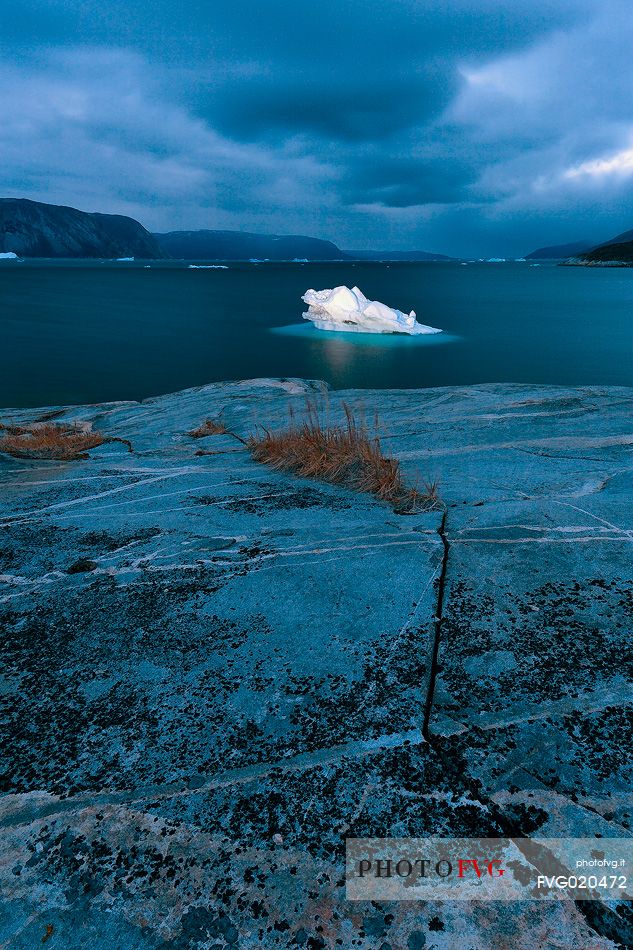 Dark clouds above iceberg in the sea in front  of Ataa a small village of fishermen and seal hunters which was abandoned in the 50s