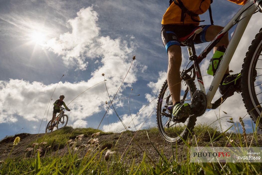 Two young mountain bikers come down from Biscia summit, in the background the Sesto Dolomites, Cadore, Italy