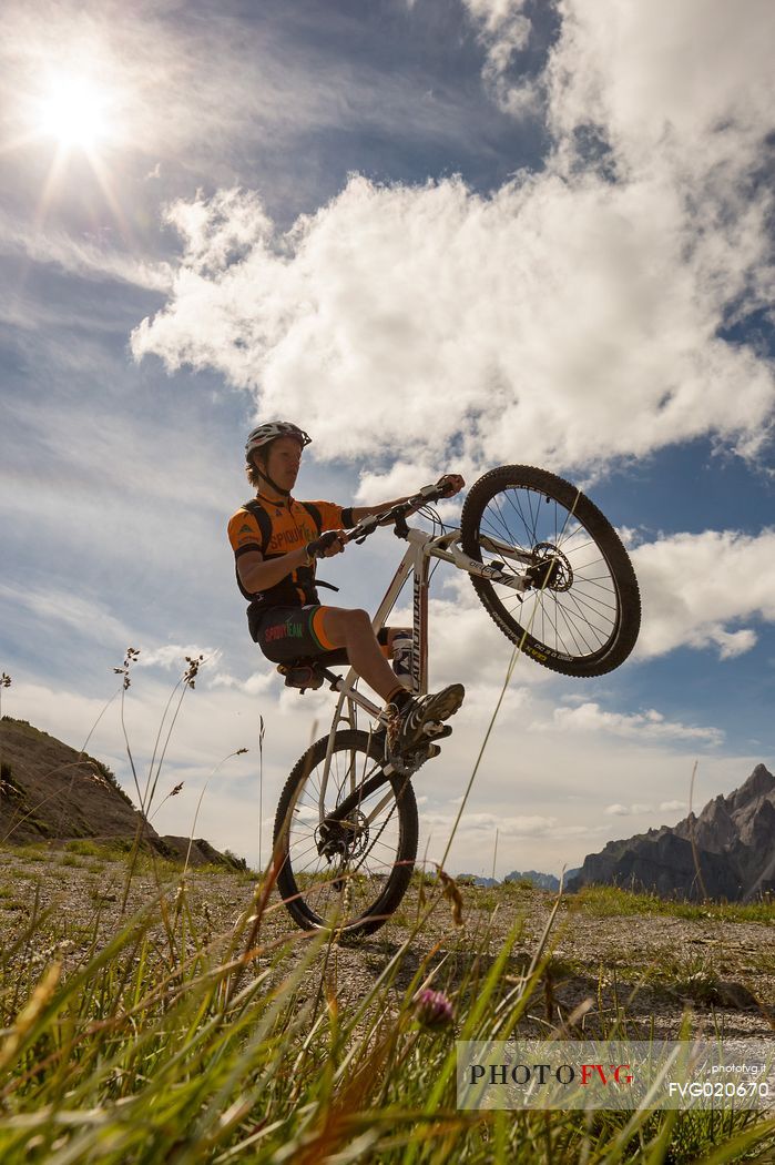 Two mountain bikers come down from Biscia summit, in the background the Sesto Dolomites, Cadore, Italy