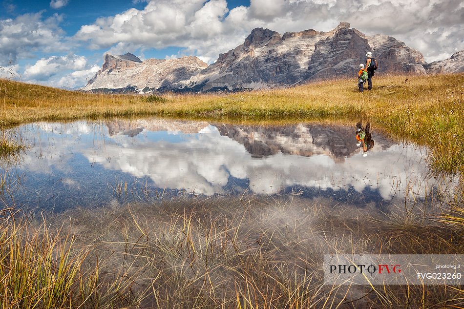 Hikers at lake in Pralongi meadows, in background the Sasso della Croce mountain, Val Badia, Dolomites, South Tyrol, Italy 