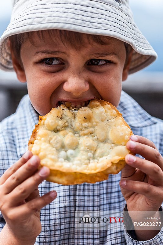 Hungry child eats Turtres, traditional ladin food, South Tyrol, Dolomites, Italy