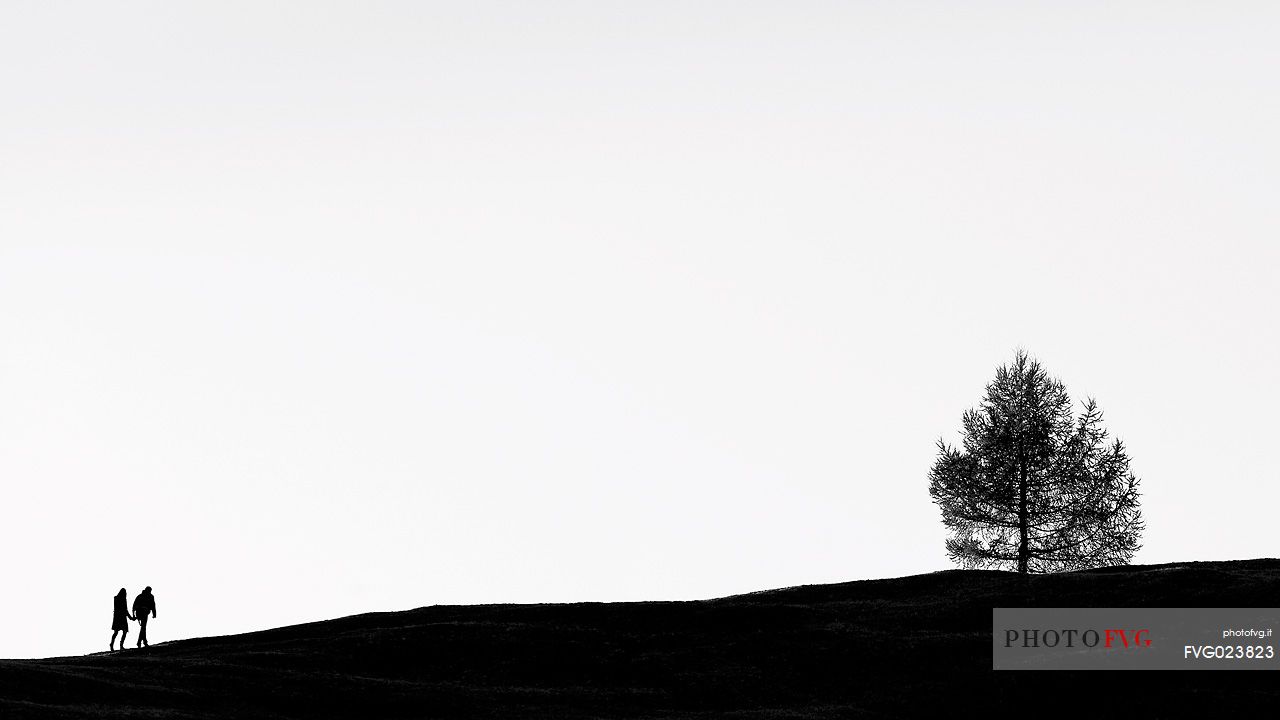 Silhouette coupe hiking along a path of Prati dell'Armentara, South Tyrol, Dolomites, Italy 