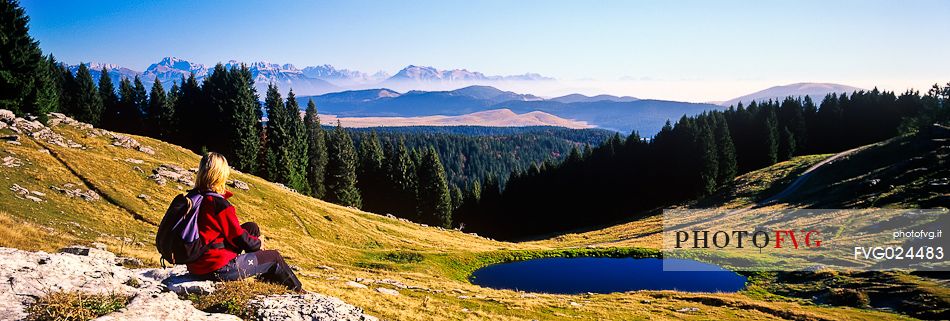 Trekker looking the landscape of  Meletta di Gallio and in the background the dolomites, Asiago, Italy