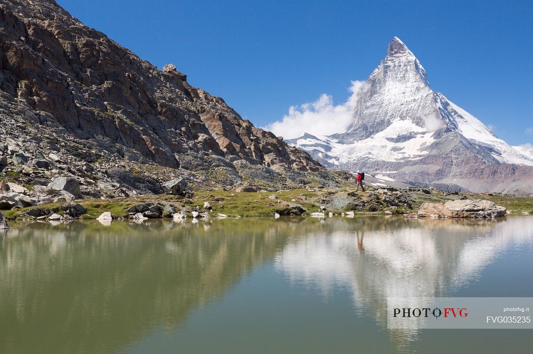 Hiker in the shore of Riffelsee Lake ( Riffel lake ), in the background the Matterhorn or Cervino mount, Zermatt, Valais, Switzerland, Europe