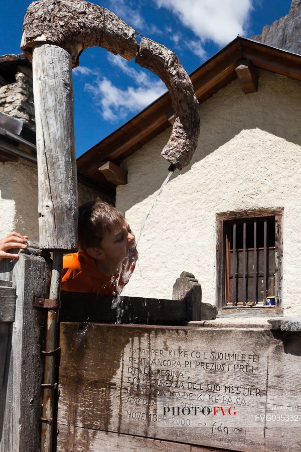 Little boy drinking from a water fountain at the Ombretta alm, Marmolada mountain group, Rocca Pietore, dolomites, Veneto, Italy, Europe