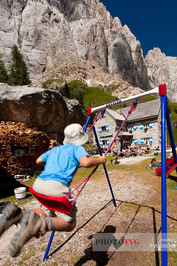 Child  swinging on seesaw at the Rifugio Falier hut, below at the south cliff of Marmolada, Val Ombretta, dolomites, Veneto, Italy, Europe